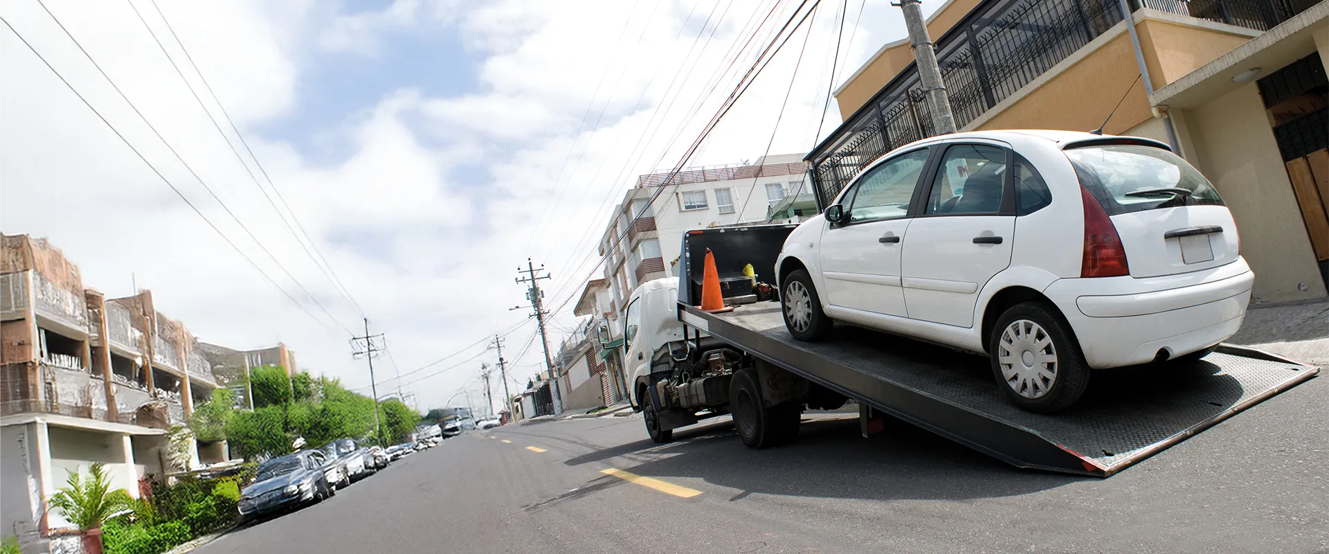 Depannage-vehicule remorque une petite voiture blanche en panne dans une rue en pente à Narbonne